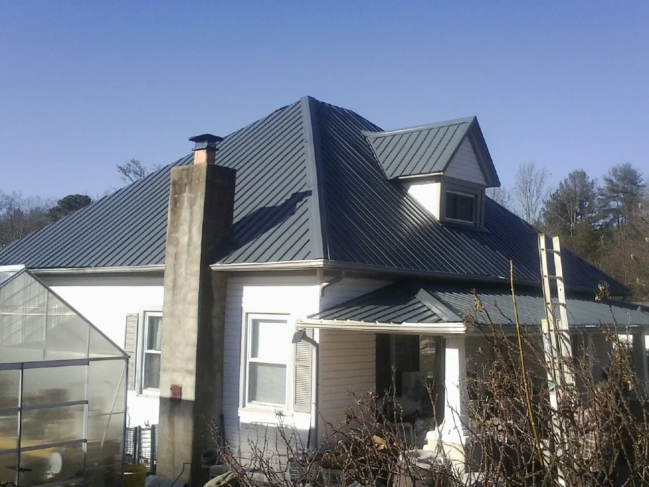 Dark blue standing seam metal roof on a white farmhouse with dormer — Slate & Tile Roof Repair by Roofing Brothers in Celina