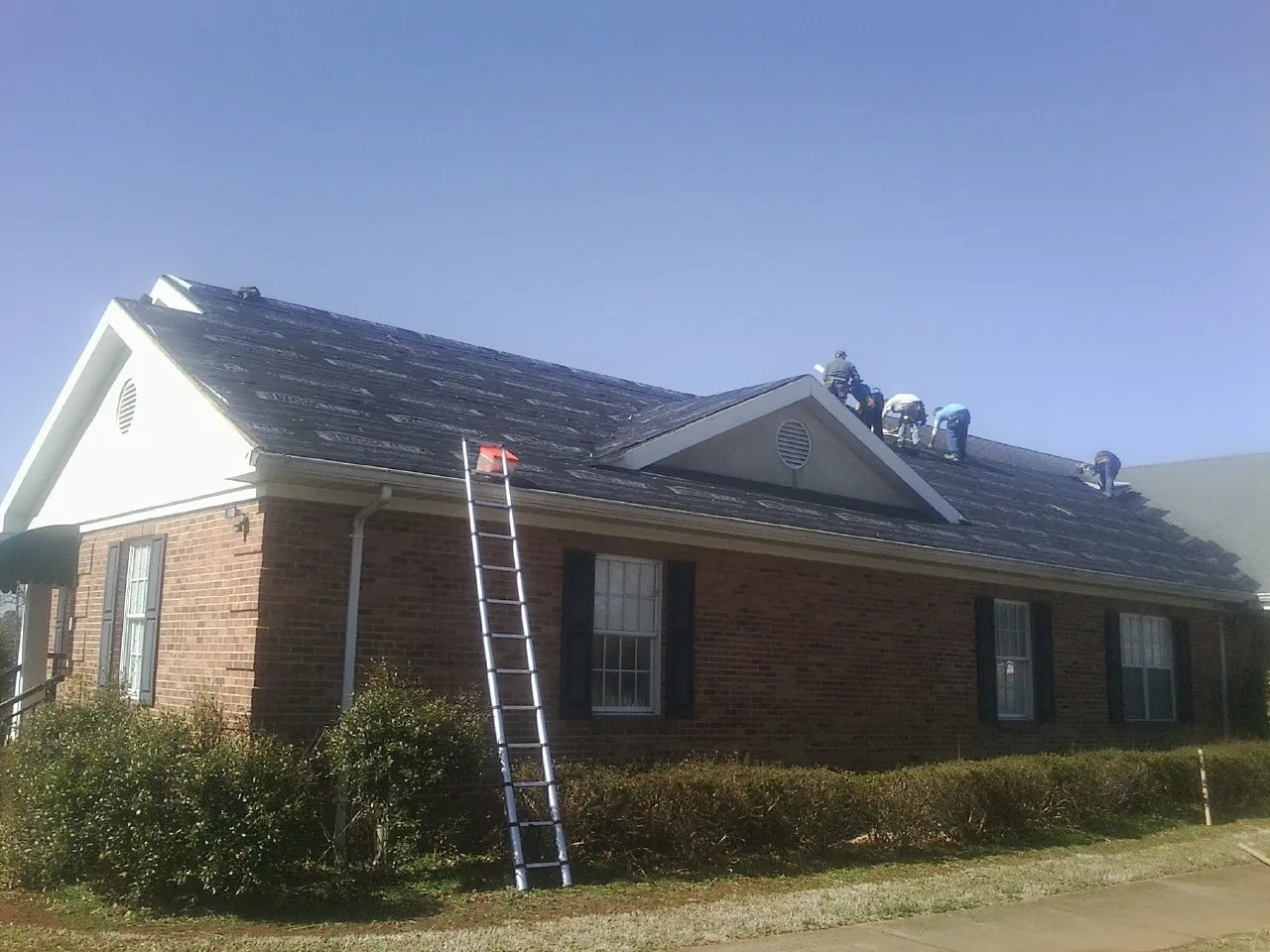 Crew tearing shingles off a brick ranch roof with a ladder set — Emergency Roof Repair work by our crew in Celina