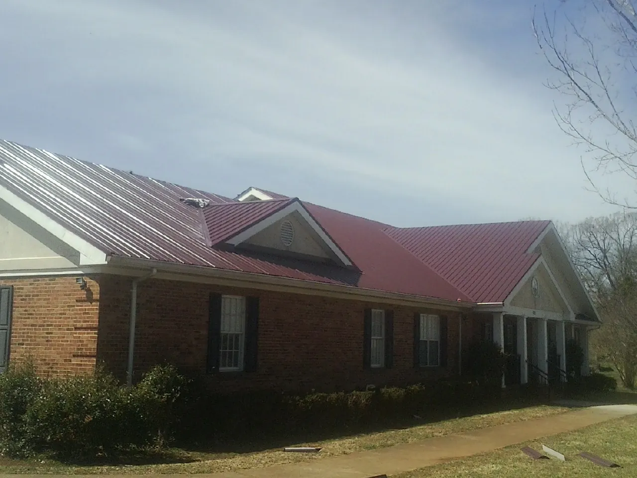 Red metal roof with gabled entries on a long brick building, from a Hail Damage Roof Repair job in Celina